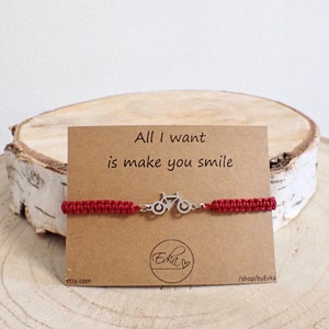 May include: A red macrame bracelet with a silver bicycle charm. The bracelet is displayed on a brown card with the text "All I want is make you smile". The card also includes the Etsy shop name.