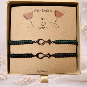 May include: A gift box containing two matching bracelets. One bracelet is dark green, the other is black. Each bracelet has a wine glass charm. The card inside the box reads "Partners in wine" with wine glass illustrations.