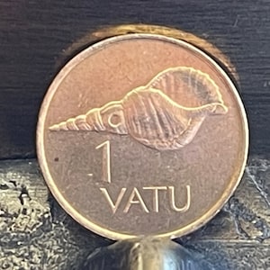 Peut inclure: Une pièce de monnaie de couleur cuivre avec un motif de coquillage et le texte "1 VATU" dessus.