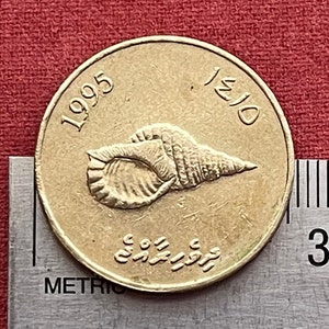 Peut inclure: Une pièce de monnaie dorée avec un motif de coquillage et l'année 1995 d'un côté et le nombre 10/50 de l'autre.