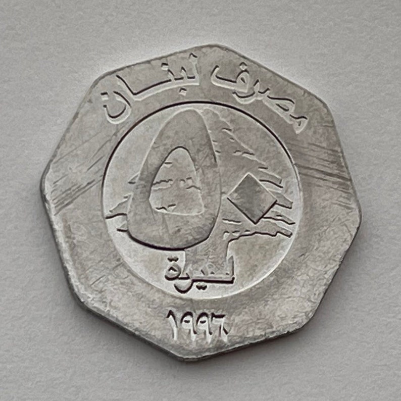 May include: A silver coin with the year 1997 and Arabic text on it. The coin features a stylized image of a cedar tree, a symbol of Lebanon.
