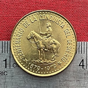 May include: Gold-colored coin with the text "CENTENARIO DE LA CONQUISTA DEL DESIERTO 1879-1979" and a depiction of a person on horseback.