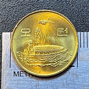 May include: A gold-coloured Korean coin featuring the text "1 Won" and an image of a traditional Korean ship with oars.