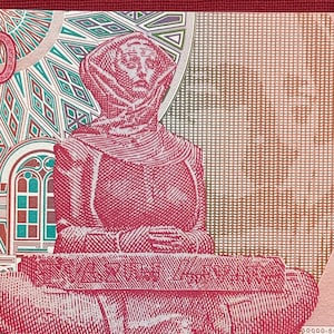 Op de afbeelding: Een close-up van een roze en witte bankbiljet met een portret van een man die een gekapte robe draagt. De man zit met zijn handen in zijn schoot. Het bankbiljet heeft een patroonachtige achtergrond met een geometrisch ontwerp.