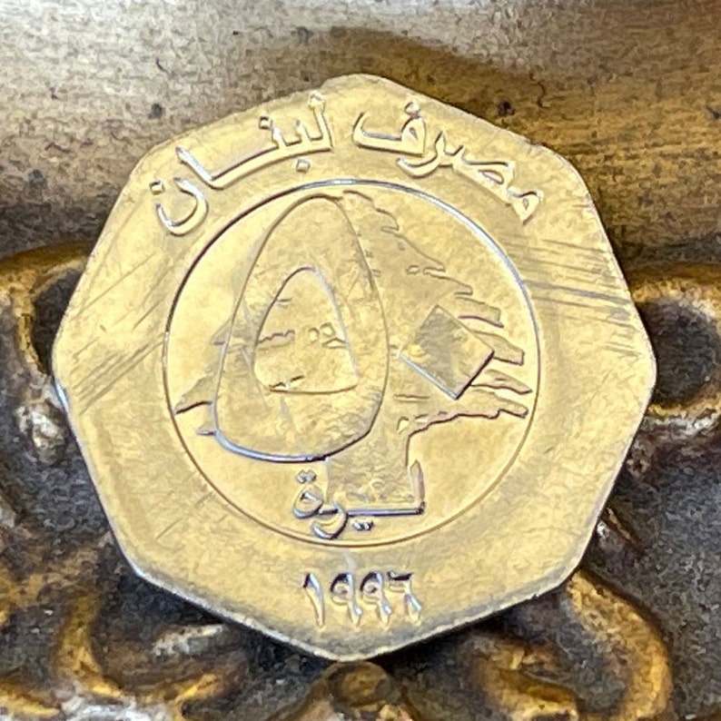 May include: A silver-colored coin with the Lebanese cedar tree and the year 1997 inscribed on it. The coin also features the Arabic text "جمهورية لبنان" which translates to "Republic of Lebanon".