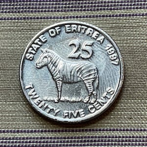 Puede incluir: Una moneda de plata con una cebra en el anverso y el texto "State of Eritrea 1993 Twenty Five Cents" alrededor del borde. El número "25" está en el centro de la moneda.