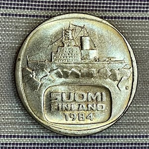 May include: A silver Finnish coin with a ship breaking through ice and the text "SUOMI FINLAND 1984" on the back.