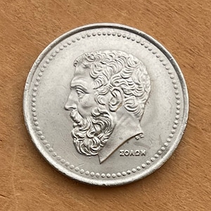 May include: Silver Greek coin featuring a profile of Solon, a Greek statesman, with the inscription "SOLON" in Greek letters.