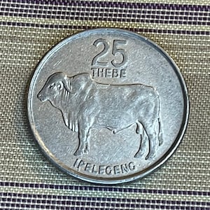 Puede incluir: Una moneda de plata con una imagen de una vaca y el texto "25 THEBE" e "IPELECENG".