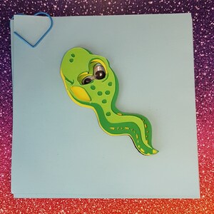 Pode incluir: Um recorte de feltro verde e amarelo de uma criatura de desenho animado com olhos saltitantes. A criatura tem um corpo longo e fino e uma cabe&ccedil;a redonda.
