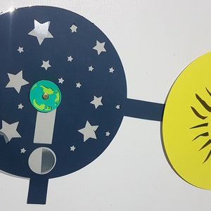 May include: A blue and silver cardboard disc with stars and a half moon, connected to a yellow disc with a black sun. The blue disc has a small green globe in the center.