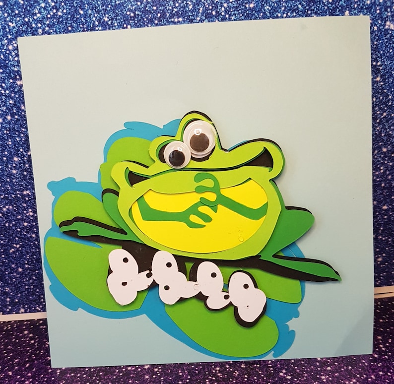 Pode incluir: Um sapo verde com olhos saltitantes senta-se em um l&iacute;rio d'&aacute;gua verde com bolinhas brancas. O sapo est&aacute; sorrindo e tem os bra&ccedil;os cruzados. O l&iacute;rio d'&aacute;gua est&aacute; em um fundo azul.