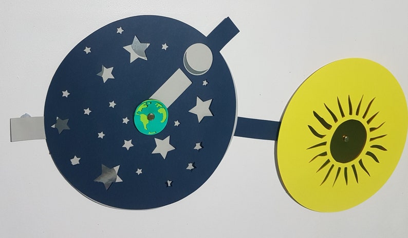 May include: A blue paper plate with a white paper moon, a small green paper Earth, and silver stars. A yellow paper plate with a black paper sun is attached to the blue plate with a black paper strip.