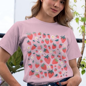 K&ouml;nnte beinhalten: Ein pinkfarbenes T-Shirt mit einem Muster aus roten Erdbeeren und wei&szlig;en Bl&uuml;ten.