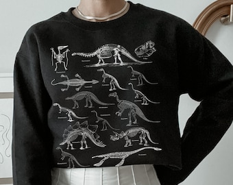 Op de afbeelding: Zwart gecropped sweatshirt met een witte print van dinosaurus skeletten. Het sweatshirt heeft een ronde hals en lange mouwen.