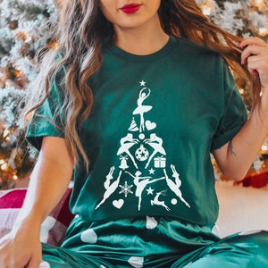 May include: A green t-shirt with a white design of a Christmas tree made up of dancers. The tree is decorated with ornaments, stars, and a reindeer.