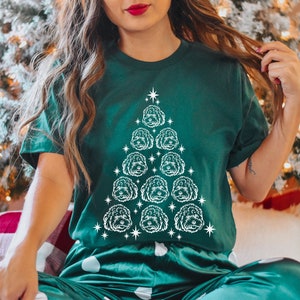 May include: A green t-shirt with a white outline of a Christmas tree made of dog faces. The tree is decorated with white stars.