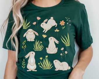 May include: A dark green t-shirt with a pattern of white bunnies and yellow flowers. The bunnies are in various poses, some sitting, some standing, and some hopping. The flowers are scattered throughout the design.