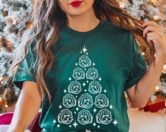 May include: A green t-shirt with a white outline of a Christmas tree made of dog faces. The tree is decorated with white stars.