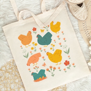 May include: A beige tote bag with a colorful design of chickens and flowers. The chickens are orange, yellow, and teal. The flowers are red, pink, and yellow.