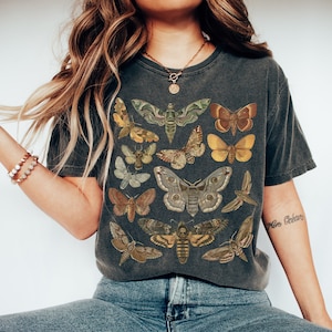 May include: A dark gray t-shirt with a vintage print of various moths and butterflies in shades of brown, yellow, and green. The shirt has a crew neck and short sleeves.