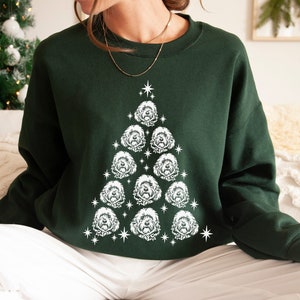 May include: A green sweatshirt with a white Christmas tree design featuring a pattern of dog faces. The tree is decorated with white stars.