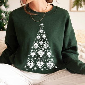 Puede incluir: Una sudadera verde con un dise&ntilde;o de &aacute;rbol de Navidad blanco con m&uacute;ltiples caras de perros husky. El &aacute;rbol est&aacute; decorado con estrellas blancas.