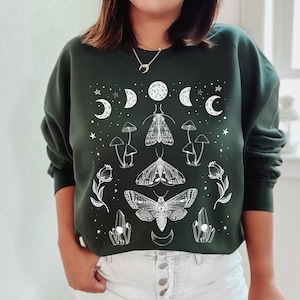 May include: A dark green sweatshirt with a white graphic print of moths, mushrooms, crystals, and crescent moons.