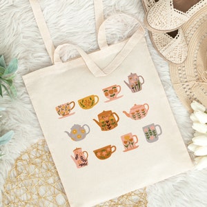 May include: A white canvas tote bag with a floral design featuring teacups and teapots in various colors and patterns. The bag has two long handles.