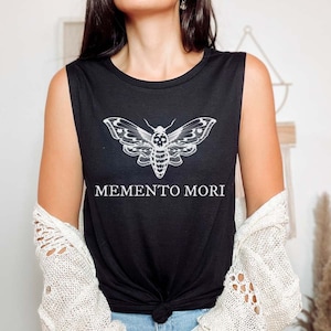 May include: Black sleeveless muscle tank top with a white graphic of a moth with a skull design and the text "MEMENTO MORI" printed below the moth.