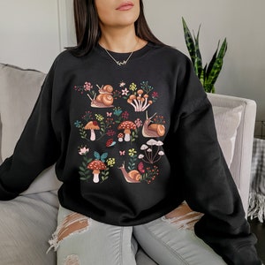 Puede incluir: Sudadera negra con un estampado gr&aacute;fico colorido de caracoles, setas y flores.