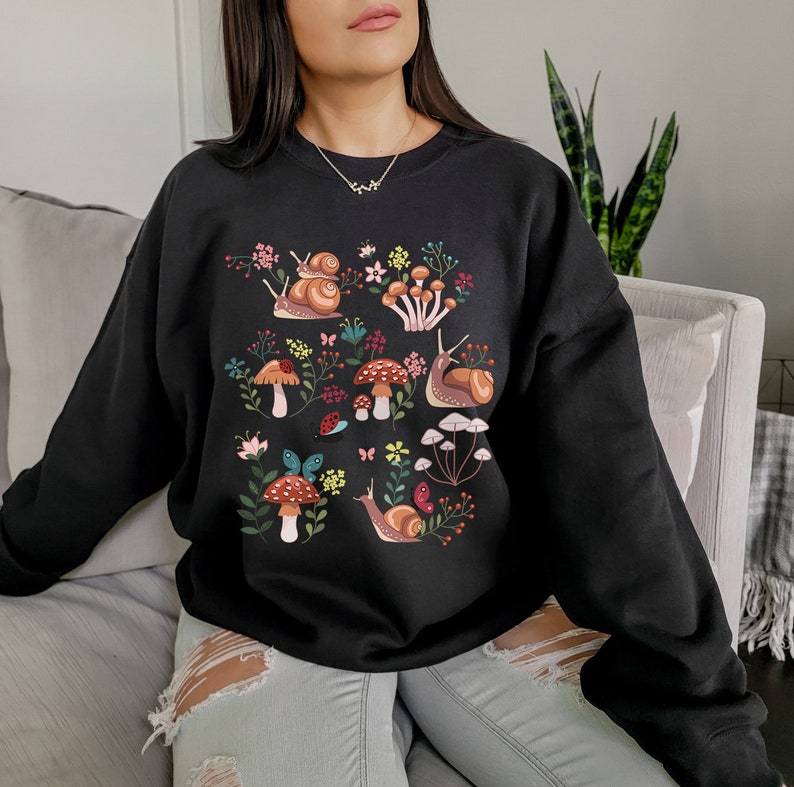 Puede incluir: Sudadera negra con un estampado gr&aacute;fico colorido de caracoles, setas y flores.