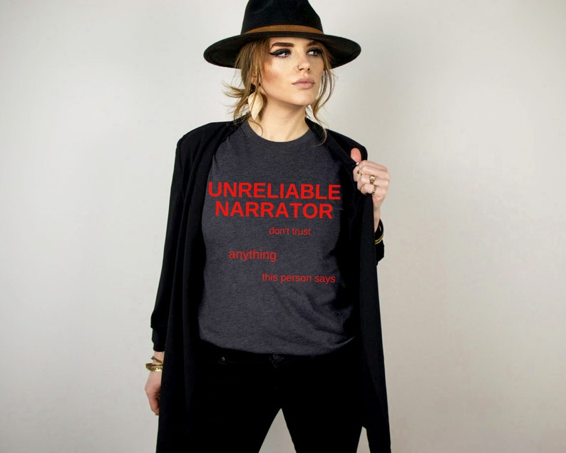 Puede incluir: Una camiseta gris oscuro con el texto "UNRELIABLE NARRATOR don't trust anything this person says" en rojo.