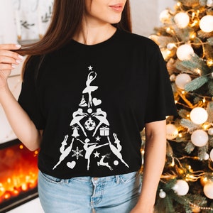 May include: A black t-shirt with a white design of a Christmas tree made up of dancers and Christmas ornaments. The tree is topped with a star.