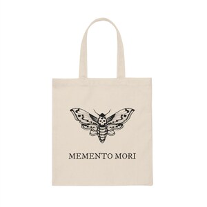 May include: A beige tote bag with a black and white moth design and the text "MEMENTO MORI" printed on the front.