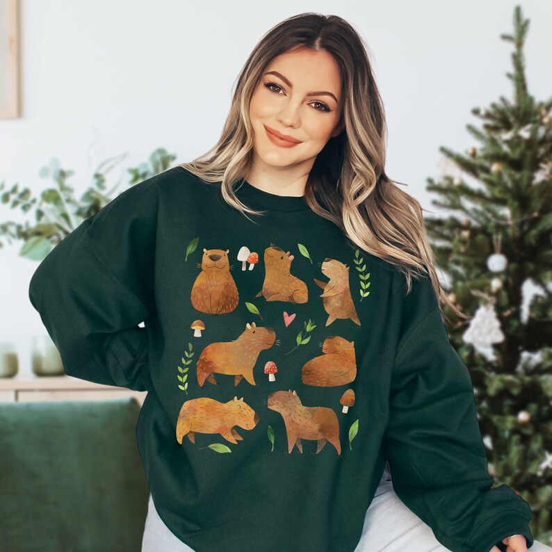 May include: A dark green sweatshirt with a pattern of brown capybaras and mushrooms. The capybaras are in various poses, including sitting, standing, and lying down. The mushrooms are red and white.