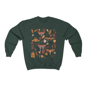 Puede incluir: Una sudadera verde oscuro con un patr&oacute;n colorido de polillas, cristales y flores. Las polillas son de varios tonos de naranja, marr&oacute;n y rosa.