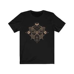 May include: Black t-shirt with a brown butterfly graphic design. The butterfly is surrounded by a geometric pattern and crescent moons.