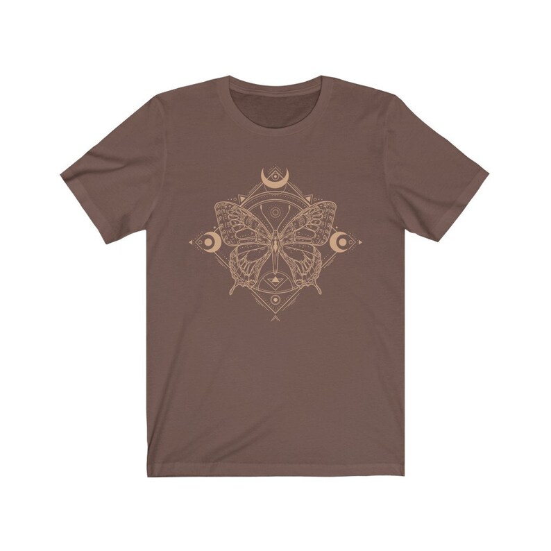 May include: A brown t-shirt with a geometric design featuring a butterfly and crescent moons in a beige color.