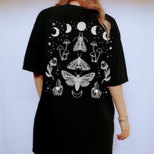 Op de afbeelding: Zwart oversized T-shirt met een witte grafische print van motten, paddenstoelen, kristallen en halve manen.