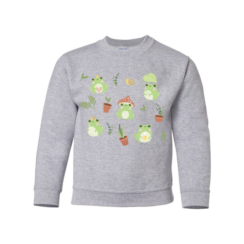 K&ouml;nnte beinhalten: Ein graues Sweatshirt mit einem Muster aus gr&uuml;nen Fr&ouml;schen, Pflanzen und Pilzen. Die Fr&ouml;sche tragen Kronen, H&uuml;te und halten Blumen.