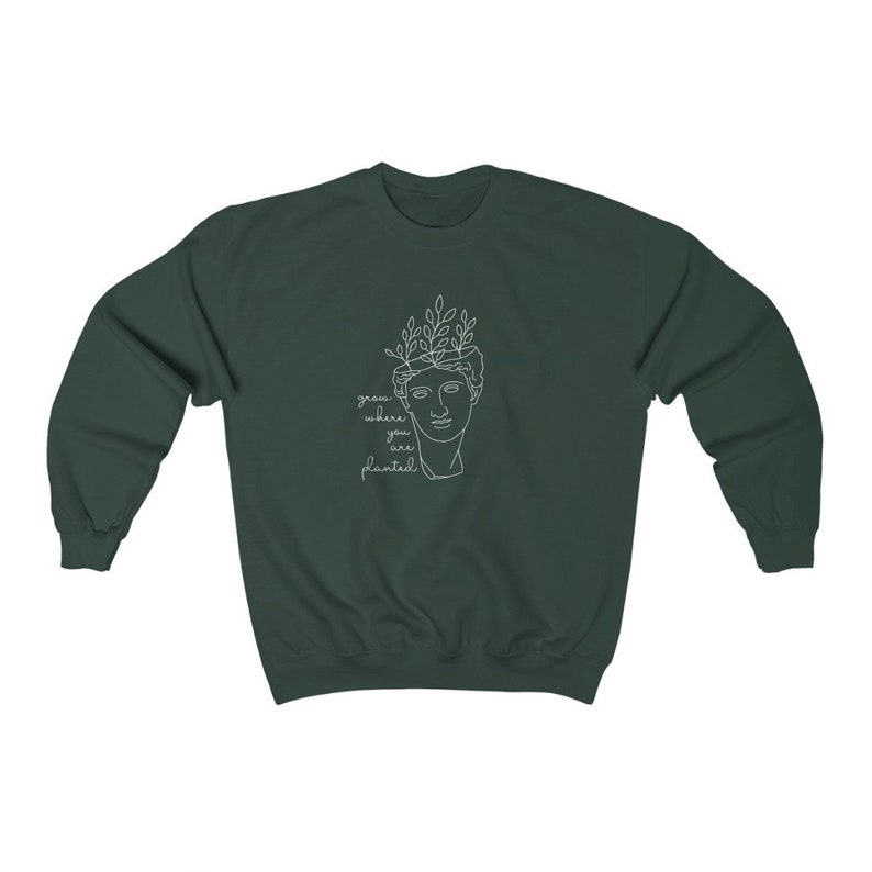 May include: A dark green sweatshirt with a white outline of a person's head with leaves on top. The text "grow where you are planted" is written below the image.