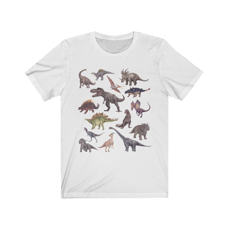May include: White t-shirt with a colorful illustration of various dinosaurs, including a Tyrannosaurus Rex, Triceratops, Stegosaurus, and Pterodactyl.