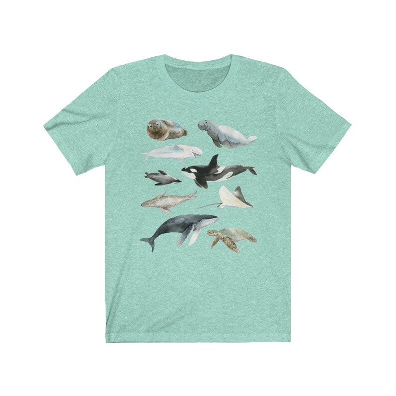 K&ouml;nnte beinhalten: Ein blaugr&uuml;nes T-Shirt mit einer Aquarell-Illustration verschiedener Meerestiere, darunter ein Wal, ein Delfin, eine Meeresschildkr&ouml;te, ein Rochen und eine Robbe. Die Illustration ist in Graut&ouml;nen, Schwarz und Wei&szlig; gehalten.