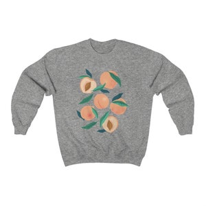 K&ouml;nnte beinhalten: Ein graues Sweatshirt mit einem Grafikdruck von Pfirsichen mit gr&uuml;nen Bl&auml;ttern. Die Pfirsiche sind hellorange.