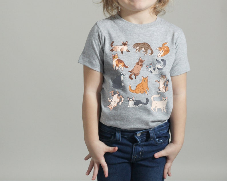 May include: A gray t-shirt with a print of various cats in different poses. The cats are in shades of gray, white, orange, and brown.