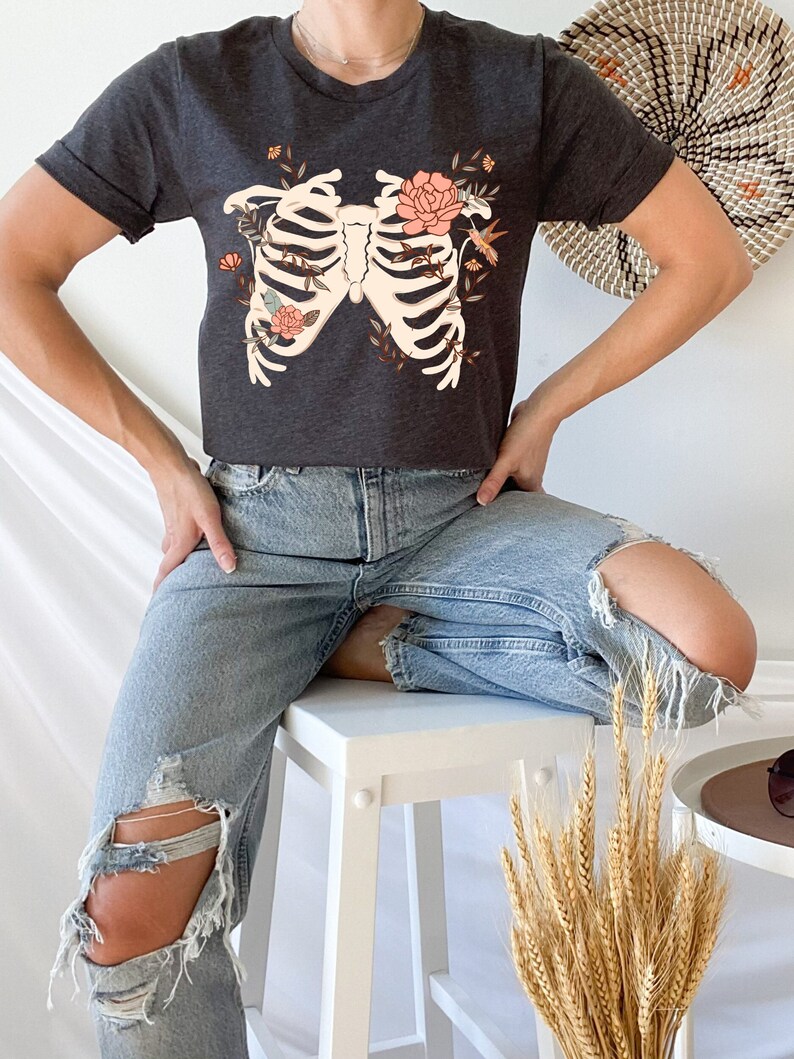 May include: A dark gray t-shirt with a floral ribcage design. The design features a white ribcage with pink flowers and a hummingbird.