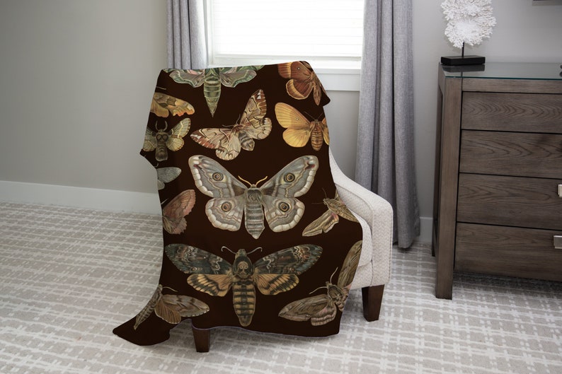 May include: A brown throw blanket with a repeating pattern of colorful butterflies and moths. The blanket is draped over a chair.