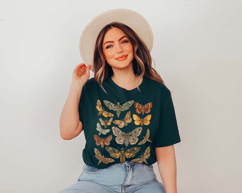 May include: A dark green t-shirt with a print of various butterflies and moths in shades of brown, yellow, and green. The shirt has a crew neck and short sleeves.