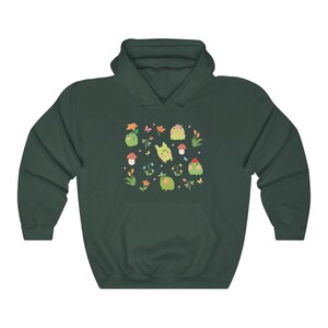 May include: A dark green hooded sweatshirt with a pattern of green frogs, flowers, and mushrooms. The frogs are wearing hats and some are holding flowers.